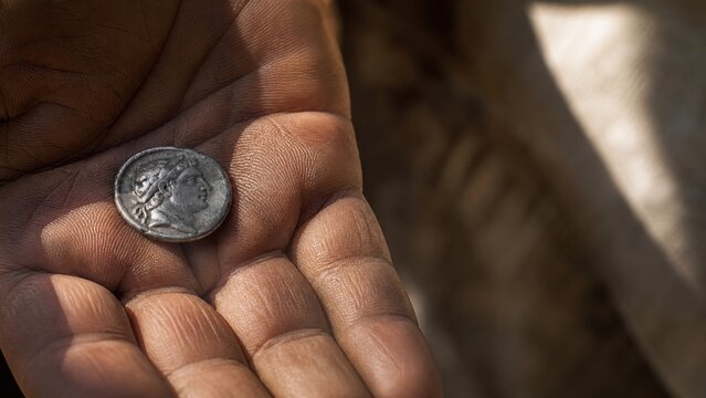 Worn ancient silver denarius with caesar portrait resting in open palm. Biblical render unto caesar concept about tax tribute and faith. Historical religious teaching symbol