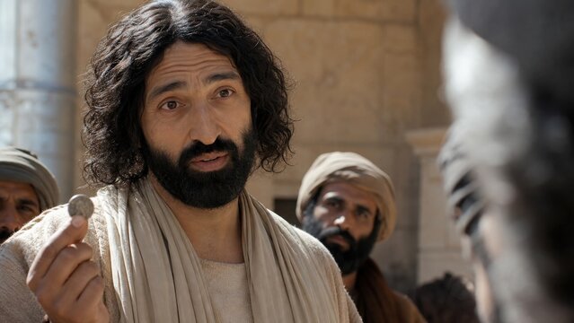 Man holding silver denarius coin at eye level asking whose image is on it in ancient temple courtyard. Biblical teaching about render to caesar and give to god, faith and wisdom concept