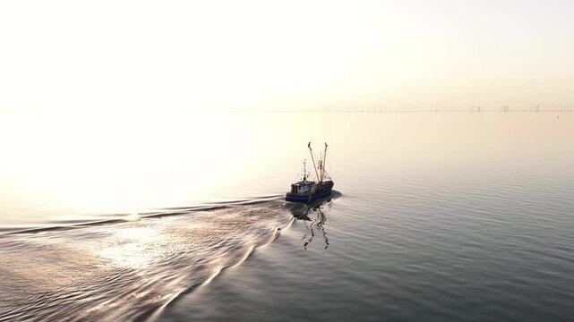 Fishing trawler navigating calm sea at sunrise