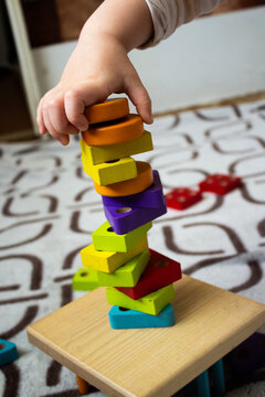 Toddler hand building or balancing unstable tower with colorful wooden blocks close up