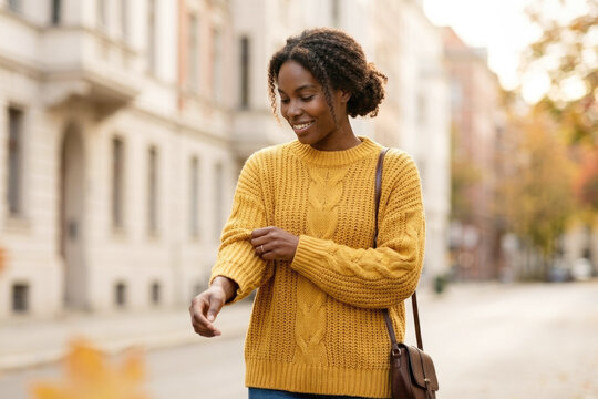 Smiling young black woman rolling up sleeves while walking on city street