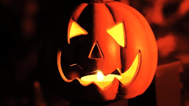 Close up of a glowing Halloween pumpkin lantern on a fence at night illustrating festive lights and warm autumn night decoration.