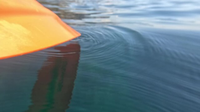 Kayak paddle water surface creates gentle ripples on the calm blue lake during a peaceful summer outdoor adventure trip