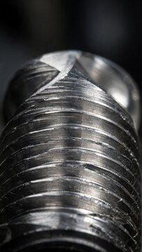 Close-up view of a metallic screw with detailed threading and a shiny surface, showcasing precision engineering and craftsmanship in a dark background setting