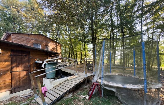 peaceful wooden cabin with trampoline in forest setting side view family vacation recreational property brown green natural light clean background copy space editorial educational visual.