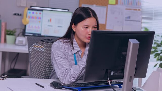 Asian woman office computer desk business employee workspace monitor keyboard professional working with calm focus seated at modern workplace interior with chart background