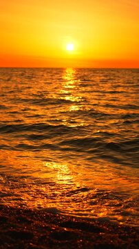 Sunset beach ocean golden sun sets over the horizon with waves gently washing over a shingle beach