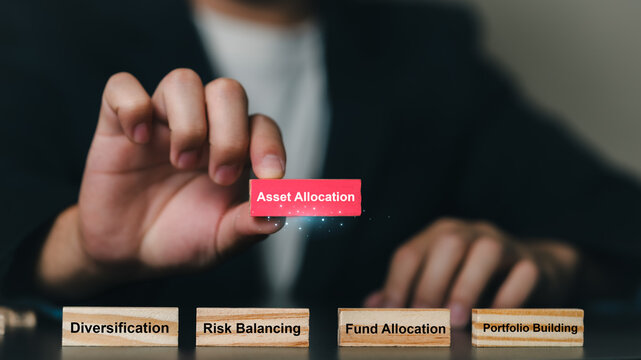 A professional dressed in formal suit holding a red card labeled Asset Allocation while standing behind wooden blocks with words like diversification, risk balancing, fund allocation