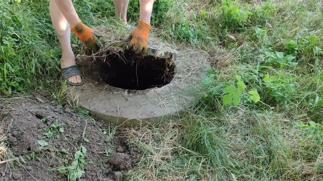 Person in orange gloves opening a grass-covered septic tank manhole in a yard