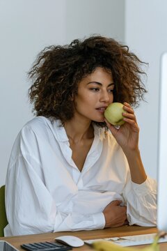 Thoughtful pregnant woman at her desk biting a green apple for maternity wellness banner and office background design