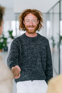 Smiling redhead man shaking hands in modern office for business meeting banner and corporate partnership background