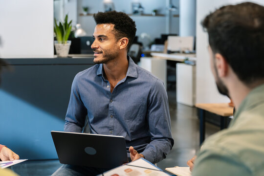 Diverse business team collaborating in a modern office, discussing strategy and sharing ideas around laptops and documents, confident professionals planning a project together