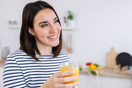 Happy young pretty woman enjoying a glass of fresh orange juice in a modern kitchen, embodying a healthy lifestyle