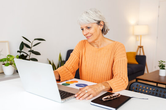 Focused senior businesswoman working on laptop at home, looking at computer screen preparing a business plan. Entrepreneur people and business concept