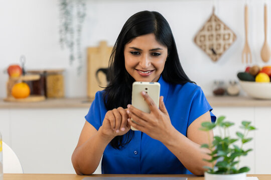 Indian woman using smartphone for online communication. Mid adult female reading messages and interacting through mobile technology. Connectivity and lifestyle concept