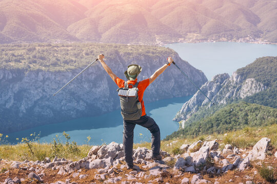 Hiker raising arms in triumph on a mountain peak overlooking a scenic Danube Iron Gates gorge and vast landscape, feeling freedom and success