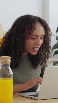 Vertical HD video of young student learning online with laptop at home. Smiling university student studying in the kitchen while enjoying breakfast and orange juice. Online education concept.