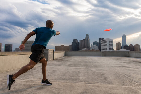Active man on a rooftop throws a frisbee toward the skyline, capturing urban outdoor sport and motion with bright daylight and a city backdrop, energetic pose and dynamic action.