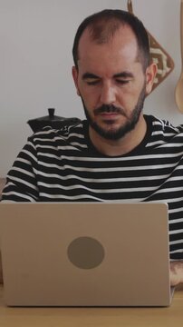 Vertical HD video of focused mid adult freelancer man working on laptop in his kitchen. He answers a phone call and then drinks a glass of water, showing remote worker day in a modern kitchen
