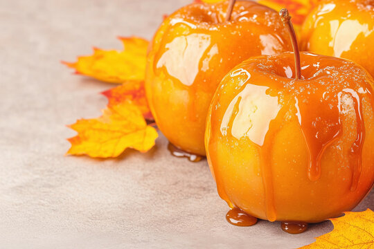 Glazed caramel apples on wooden stick with yellow maple leaves background.