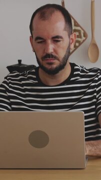 Vertical HD video of frustrated mid adult freelancer man working on his laptop in the kitchen, feeling stressed and overwhelmed by his job, showing clear signs of professional burnout at home