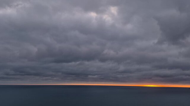Ocean sunset timelapse features dark clouds moving above a calm sea at the horizon. Static wide shot.