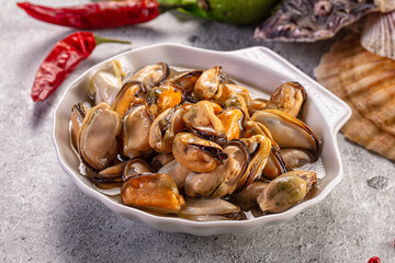 Fototapeta premium Cooked mussels in white bowl, chili peppers, seashells, grey background
