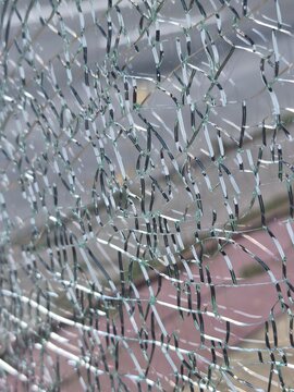 Close-up of deeply shattered transparent safety glass texture with a blurred outdoor background