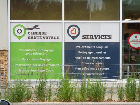 Gatineau, Quebec, Canada &ndash; June 26, 2026: Window signage displays "Clinique Sant&eacute; Voyage" and various medical services like blood tests and vaccinations behind grassy plants on Bd la V&eacute;rendrye E.