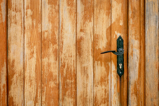 Warm-toned weathered wooden door with ornate antique iron handle and keyhole lock, offering generous copyspace. Rustic concept.