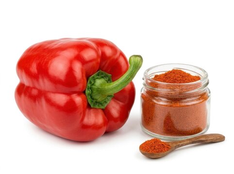 Vibrant red bell pepper with aromatic ground paprika powder in glass jar and small wooden spoon on plain white background. Bright studio lighting highlights fresh texture and culinary mood.