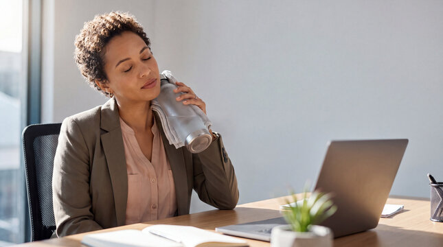 Woman holding water bottle K refreshing herself with cold drink at office desk with laptop and plant