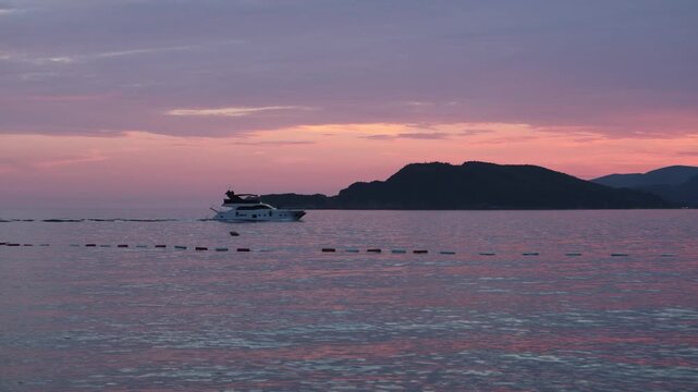 serene sunset over rocky islands with boats at dusk transitioning to night on a coastal landscape with wide angle shot and vibrant red and orange colors in the sky and sea.