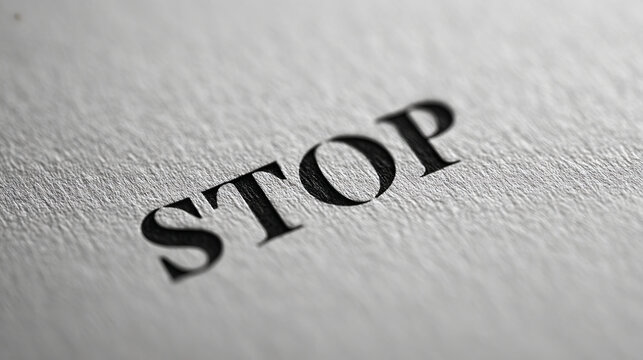 STOP word printed on textured paper with dramatic shadow and shallow depth of field, urgent concept mood