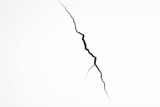 Vertical black crack splitting white wall surface. Structural damage and fracture on concrete texture. Abstract broken background with copy space for renovation and earthquake concept