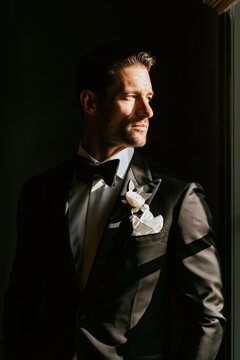 Groom standing alone before the ceremony in a classic black tuxedo, moody cinematic lighting, timeless luxury wedding portrait