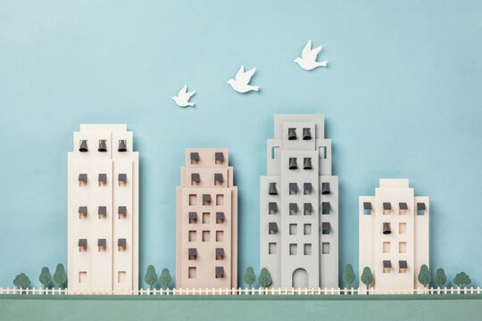 Handmade paper craft cityscape with miniature apartment buildings and flying white doves on blue background
