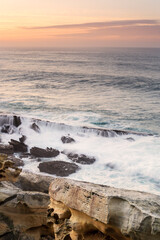 Fototapeta premium Sandstone rock formations with tafoni erosion on the coast of Jaizkibel during a dramatic sunset with long exposure ocean waves flowing over rocks in Jaizkibel, Basque Country, Spain
