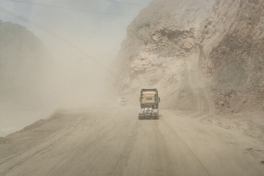 Transporting trucks with cargo along a dusty high-mountain road along the Pamir Highway, a dangerous road into a gorge, and vehicles traveling along it