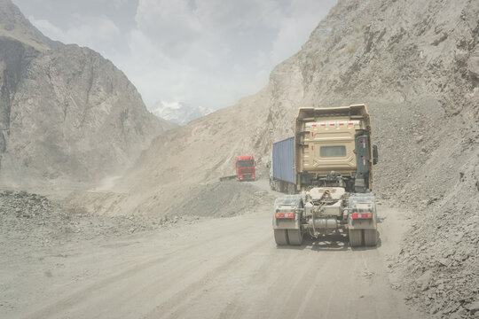 Transporting trucks with cargo along a dusty high-mountain road along the Pamir Highway, a dangerous road into a gorge, and vehicles traveling along it