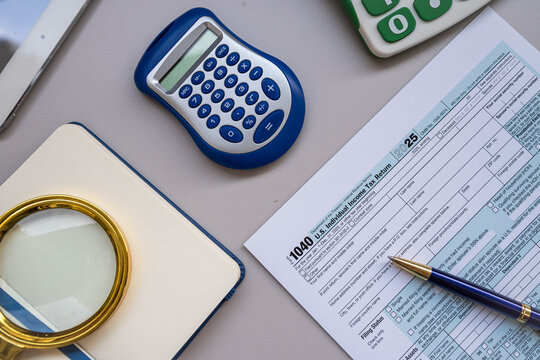 Close up of Accountant Desk with Form 1040 Tax Documents Blue Calculator and Blank Notepad