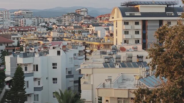 Golden hour light shines on residential buildings in a densely populated city. Solar water heaters and panels covering the rooftops