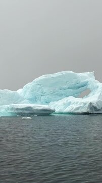 Explore the stunning beauty of gigantic icebergs in Antarctica. Gentle waves embrace these frozen giants, while soft clouds linger above, creating a serene atmosphere of nature's wonder.