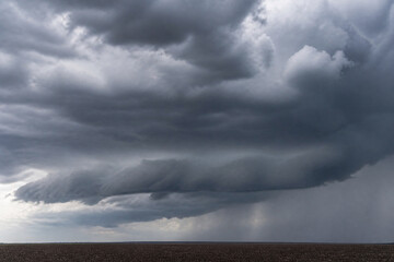 Naklejka premium Dark storm clouds covering the sky above a flat horizon. Dramatic weather scene with heavy rain clouds. Concept of severe weather, nature power, climate change, and atmospheric conditions.