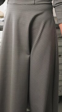 Close up of woman wearing black and white houndstooth patterned dress dark tights fluffy slippers in indoor setting. subject hands with manicured nails are visible as woman moves slightly