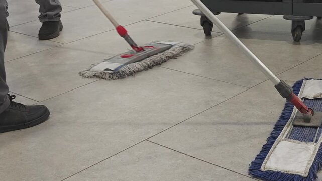 Janitorial staff performing floor cleaning duties in a commercial building. Low angle view of workers using mops for sanitizing