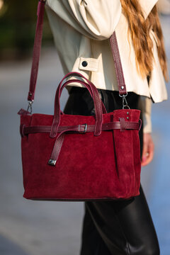 Beige trench coat paired with burgundy leather handbag and crossbody strap worn on sunny city street, showing textured fabric, polished hardware, and stylish urban fashion detail
