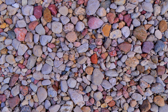 Colorful mixed pebbles and small rocks scattered across ground surface creating a natural textured background pattern with red, pink, gray, and orange tones