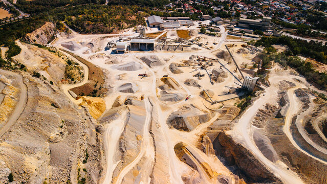 Mining site in a rural area shows operations and machinery in action. Aerial view of a mining site with machinery and large earthmoving areas during daytime.