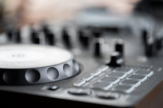 Close-up of a modern black DJ controller with a jog wheel, performance pads, and mixing knobs in selective focus